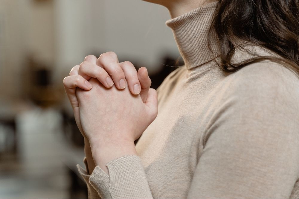 woman folding arms and praying in article confidence in religion